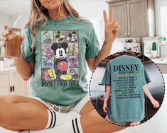 a woman in mickey mouse t - shirt and shorts holding up her peace sign while sitting on the kitchen counter