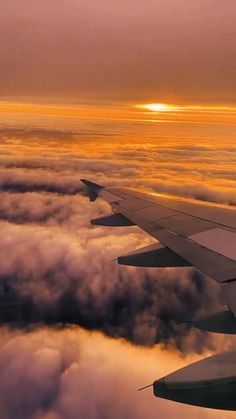 the wing of an airplane as it flies above the clouds at sunset or dawn in the sky