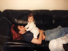 a man laying on top of a black leather couch holding a small child in his lap