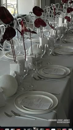 the table is set with white plates and silverware, red flowers in vases