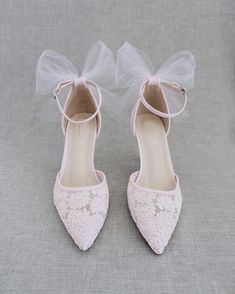 a pair of pink shoes with white lace and bows on the toes, sitting on a gray surface