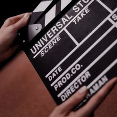 a person holding a black and white movie clapper in their right hand, with the words universal state scene take written on it