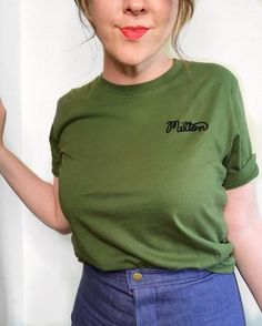 a woman wearing a green shirt and blue skirt with her hand on her hip, posing for the camera