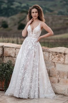 a woman in a wedding dress standing on a stone wall with her hands on her hips