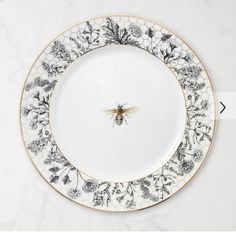 a white and black plate with a bee on the center, surrounded by flowers in gold trim