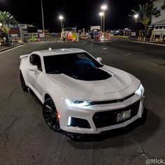 a white chevrolet camaro is parked on the side of the road at night time