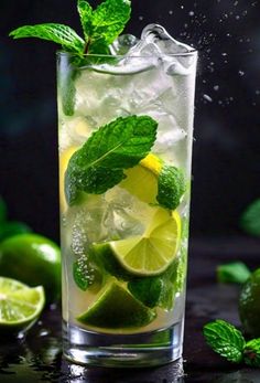 a glass filled with ice and limes on top of a table next to mint leaves