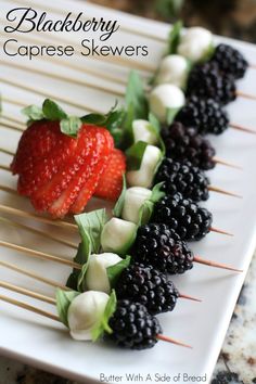 a white plate topped with strawberries and blackberries on skewers