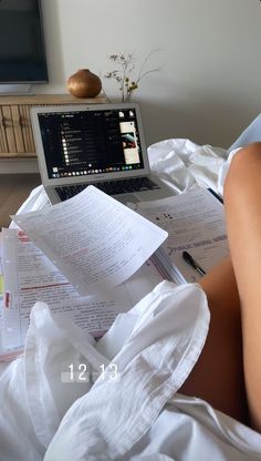 a woman laying in bed with papers and a laptop on her lap, next to the tv