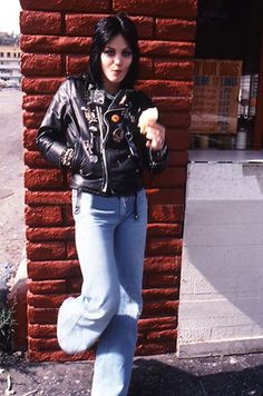 a woman leaning against a brick wall with her hand on her hip and looking at the camera