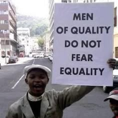 a man holding up a sign that says men of quality do not fear equality