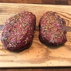 two uncooked steaks on a cutting board with sprinkles and seasoning