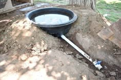 there is a large black bucket with water in it on the ground next to a tree