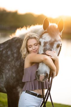 a woman is hugging a horse in front of a body of water with the sun behind her