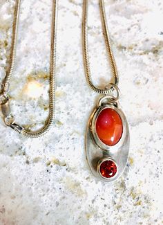 This beautiful pendant of sterling silver and 2 orange stones, one a 6mm faceted cz, and a 15 by 10mm carnelian cabochon is on an 18 inch snake chain.  It was fabricated, meaning filed, soldered, and polished to a shiny finish.  The top stone is set in a plain bezel, and the bottom, sparkly cz is set in a unique, cup-like setting, which I made by hand.  Orange is definitely my favorite warm color!  What is yours? Orange Carnelian Jewelry For Anniversary, Orange Carnelian Necklace With Round Pendant, Orange Polished Carnelian Jewelry, Unique Orange Sterling Silver Necklace, Silver Carnelian Oval Cabochon Jewelry, Polished Carnelian Orange Jewelry, Silver Carnelian Round Pendant Jewelry, Orange Sterling Silver Round Pendant Jewelry, Orange Carnelian Oval Cabochon Jewelry