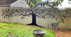 a tree painted on the side of a fence next to a yard with a chair