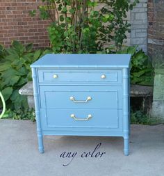 a blue dresser sitting on top of a sidewalk next to a bush and brick building