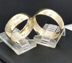 two gold wedding rings sitting on top of a black surface with clear acrylic blocks