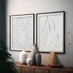 two white vases sitting on top of a wooden table in front of framed art