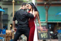 a man and woman are dancing in the street, one is wearing a red dress