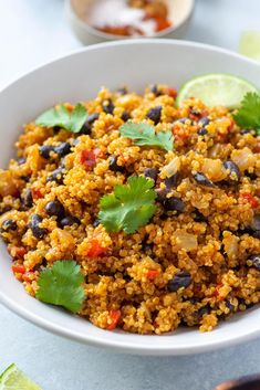 a white bowl filled with rice and black beans, cilantro leaves and lime wedges