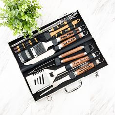 an assortment of kitchen utensils in a black box next to a potted plant