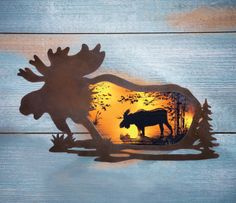 a moose is silhouetted against the setting sun in this metal wall art on wood planks