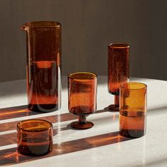 four glass vases sitting on top of a white table next to cups and glasses