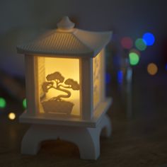 a small white lamp with a potted plant on it's side and lights in the background