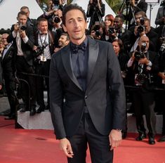 a man in a tuxedo standing on a red carpet with cameras surrounding him