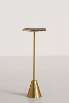 a gold metal table with a black marble top on a white surface in front of a plain wall