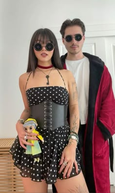 a man standing next to a woman in black and white polka dot dress holding a doll