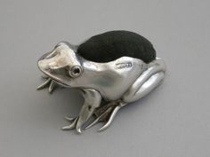 a silver frog brooch sitting on top of a gray table next to a black hat