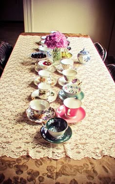 a table topped with lots of cups and saucers next to a vase filled with flowers