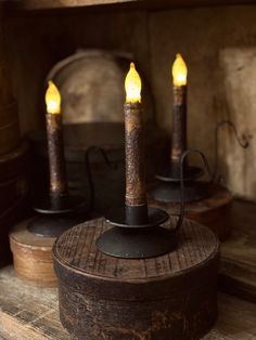 three lit candles sitting on top of a wooden box next to other wood boxes and barrels