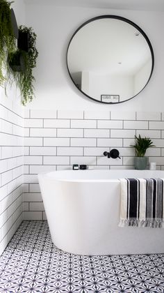 a white bath tub sitting under a round mirror in a bathroom next to a potted plant