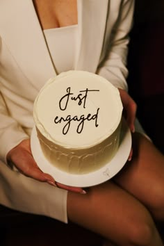 a woman holding a cake with the words just engaged written on it in cursive writing