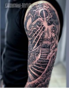 a man with a black and white tattoo on his arm is standing in front of stairs