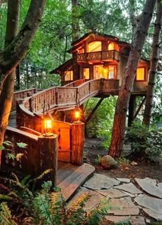 a tree house in the woods with stairs leading up to it's roof and lights on