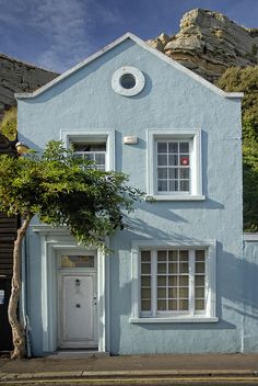 a blue house with a white door and window on the side of the street in front of a mountain