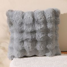 a fluffy gray pillow sitting on top of a white couch next to a wall with a plant