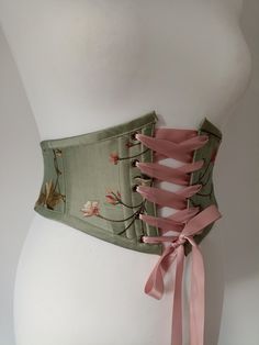 Beautiful handmade sageolive green floral silk corset belt with autumnal leaves embroideredideal for renaissance fair costume accessoryFree worldwide shipping and sent with a tracking numberSizes available are to fitXSWaist2527SWaist2829MWaist29.531.5LWaist3233.5XLWaist3435.5Crafted from gorgeous sage /olive green silk with pretty flowers and leaves embroidered all overDusky pink satin ribbon for front lacingBias binding Floral Underbust Corset, Brown Corset Belt, Moss Corset, Corset Designs Ideas, Green Underbust Corset, Sage Green Silk Dress, Fairy Belt, Corset Belt Outfit, Pretty Corset