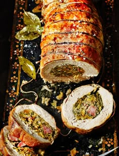 sliced meatloaf with vegetables and sauces on a black tray next to a knife