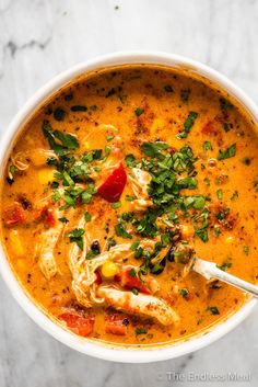 a white bowl filled with soup and garnished with green onions, tomatoes and chicken