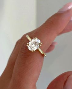 a woman's hand holding a ring with a white diamond in the middle and yellow gold band