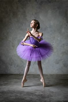 a ballerina in a purple tutu posing for the camera with her hand on her hip