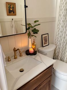 a white toilet sitting next to a bathroom sink under a mirror with a candle on it