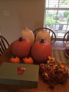 three pumpkins sitting on top of a wooden table next to a box and flowers