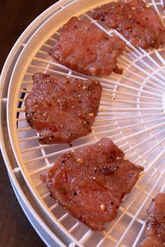 four pieces of meat sitting on top of a white plate with sauce and seasoning