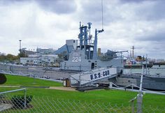 a large boat sitting in the water next to a chain link fence and green grass